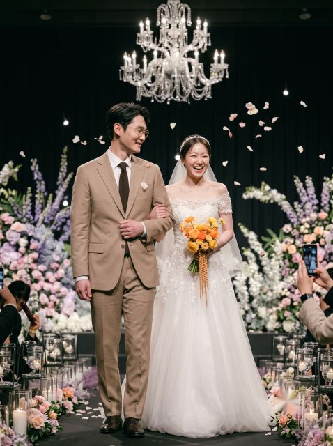 샹들리에 아래 꽃잎이 날리는 본식장에서 행진하는 신랑신부