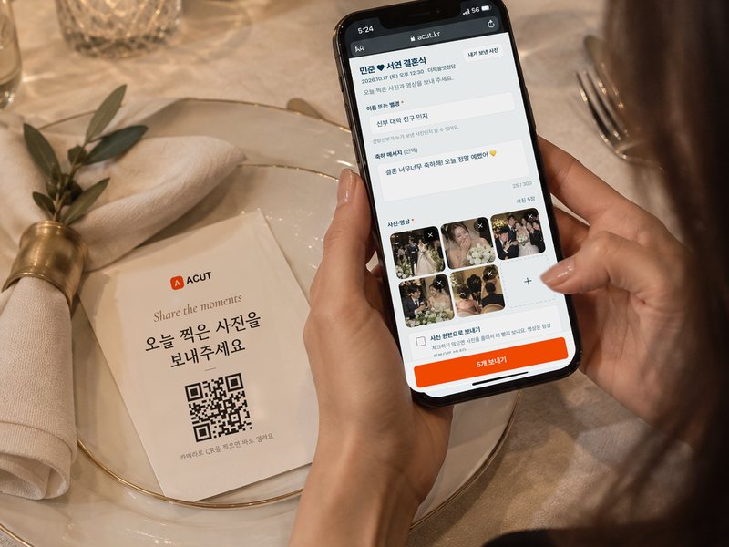 식장 테이블의 QR 안내판 옆에서 하객이 휴대폰으로 사진을 보내는 장면